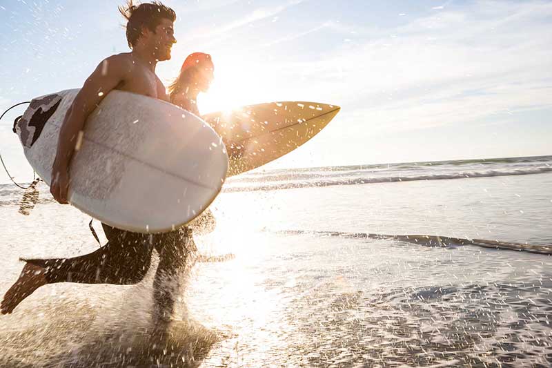 Couple running into the ocean with surfboards